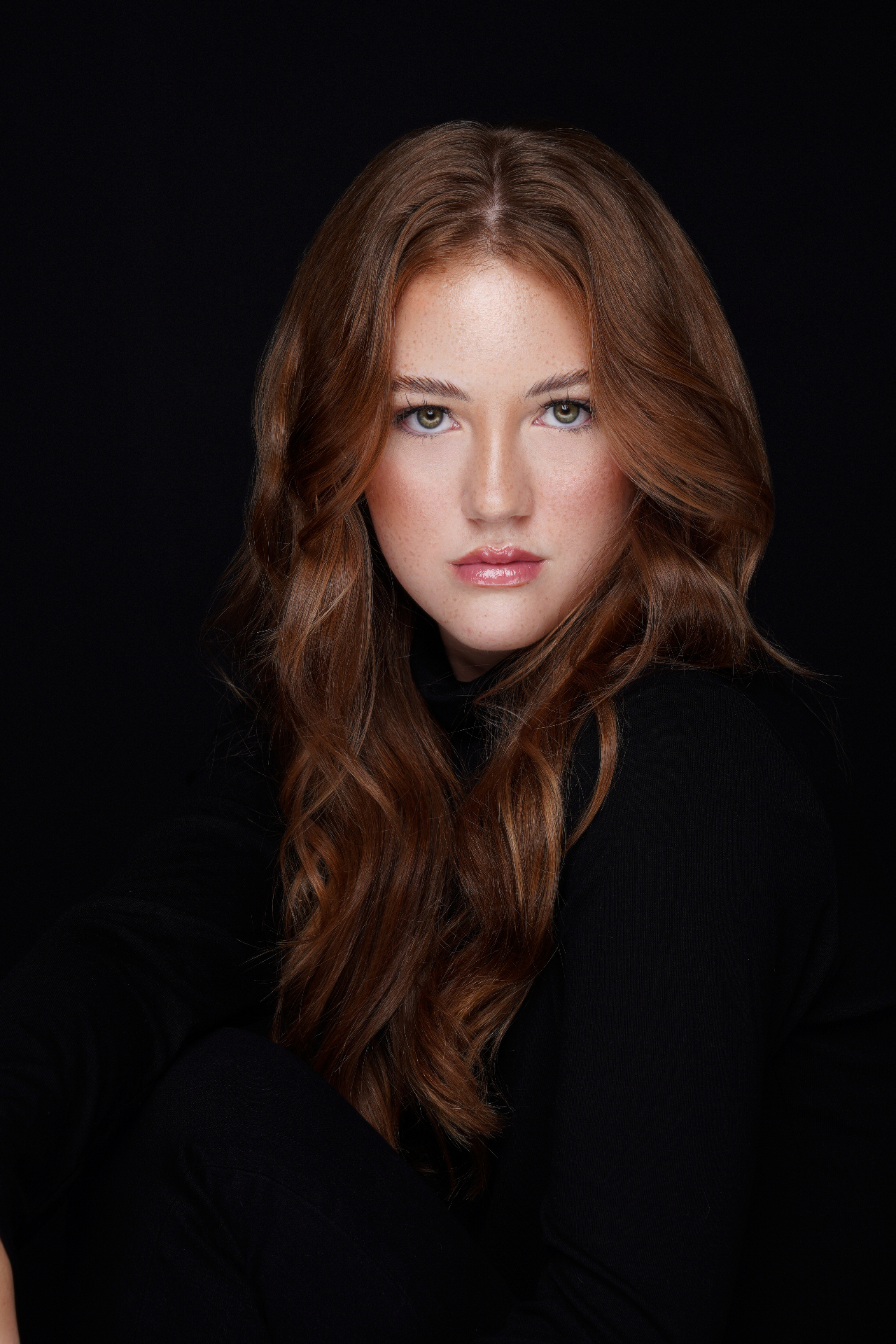Close-up studio portrait of a red-haired woman against a black background