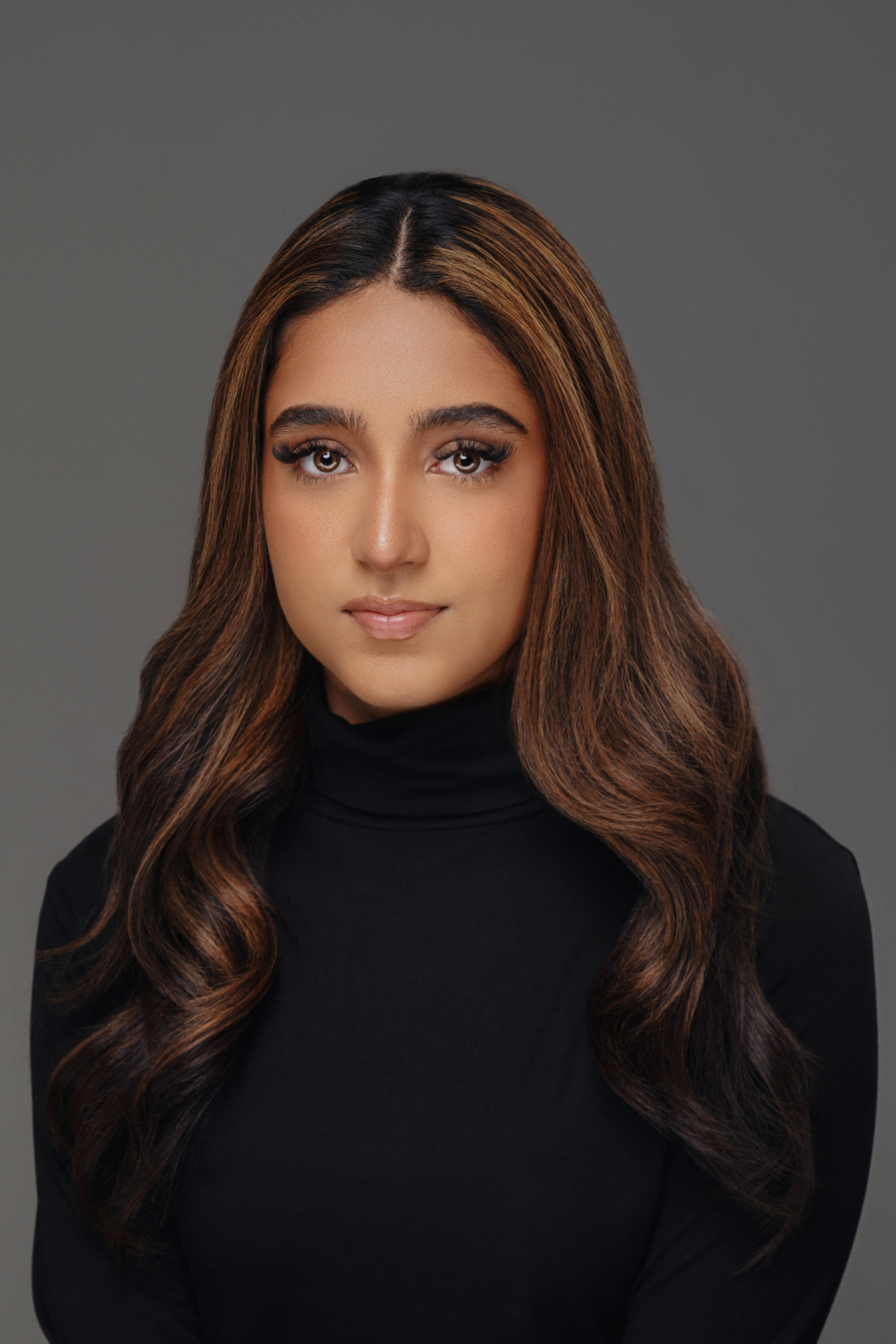 Clean studio headshot of a woman with long hair wearing a black turtleneck against a gray background