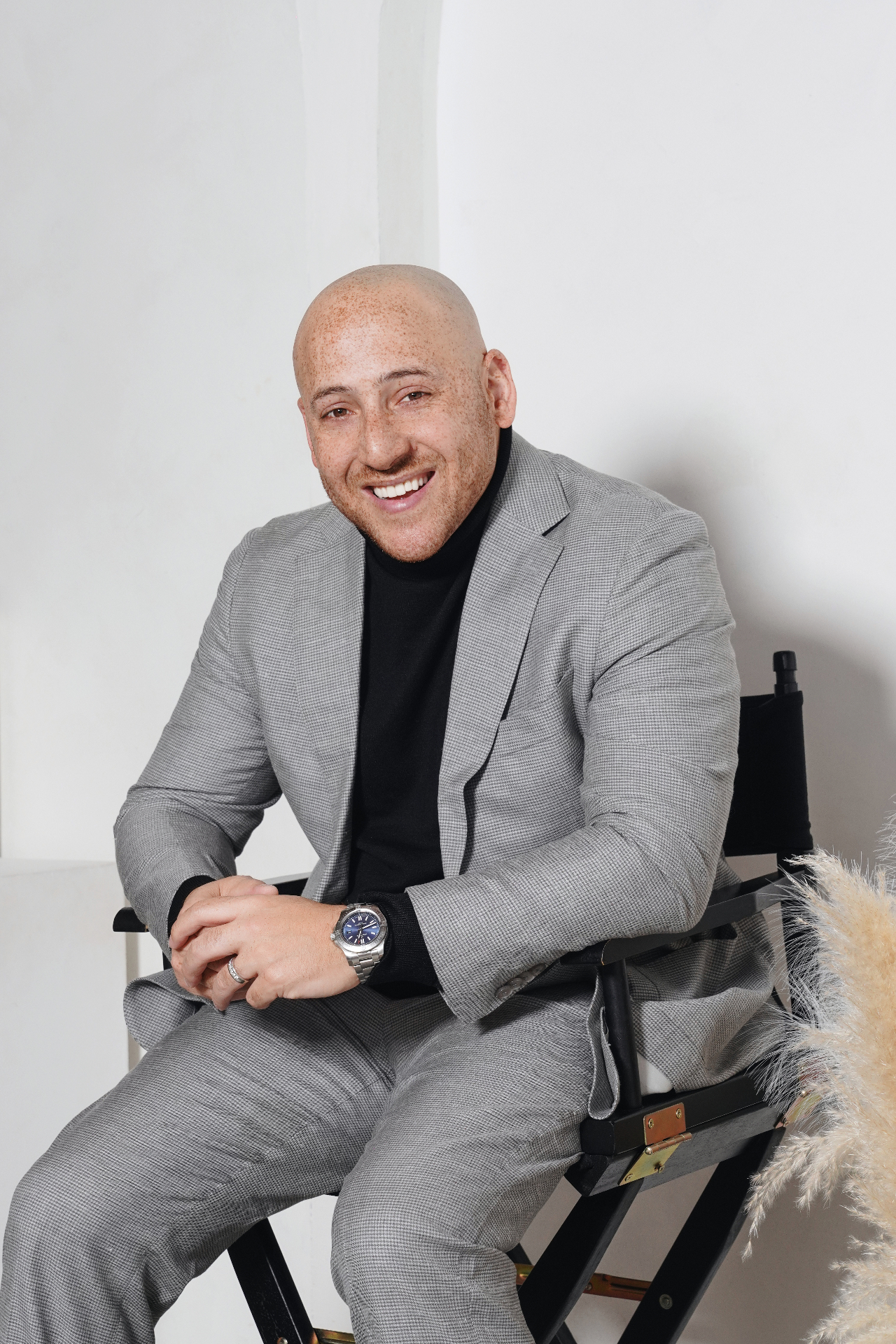 Modern indoor headshot of a smiling man in a gray suit seated in a studio chair