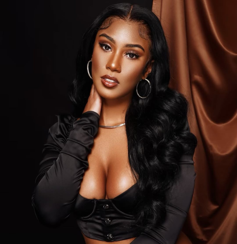 Editorial portrait of a woman with long wavy hair in a black satin top against a brown satin backdrop