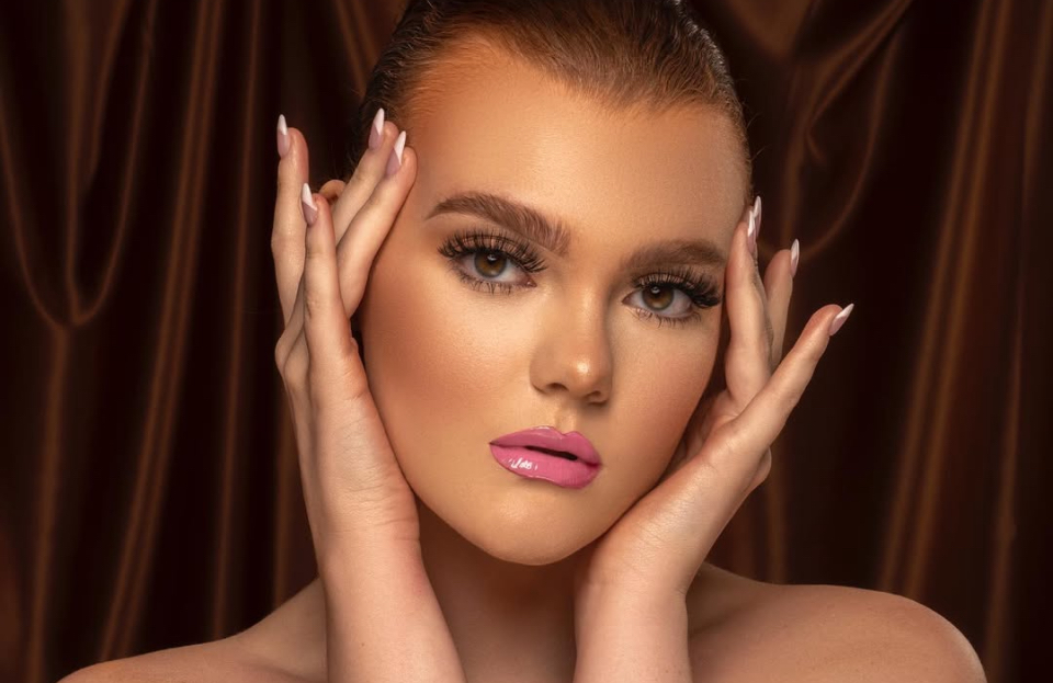Beauty portrait of a woman framing her face with her hands against a bronze satin backdrop