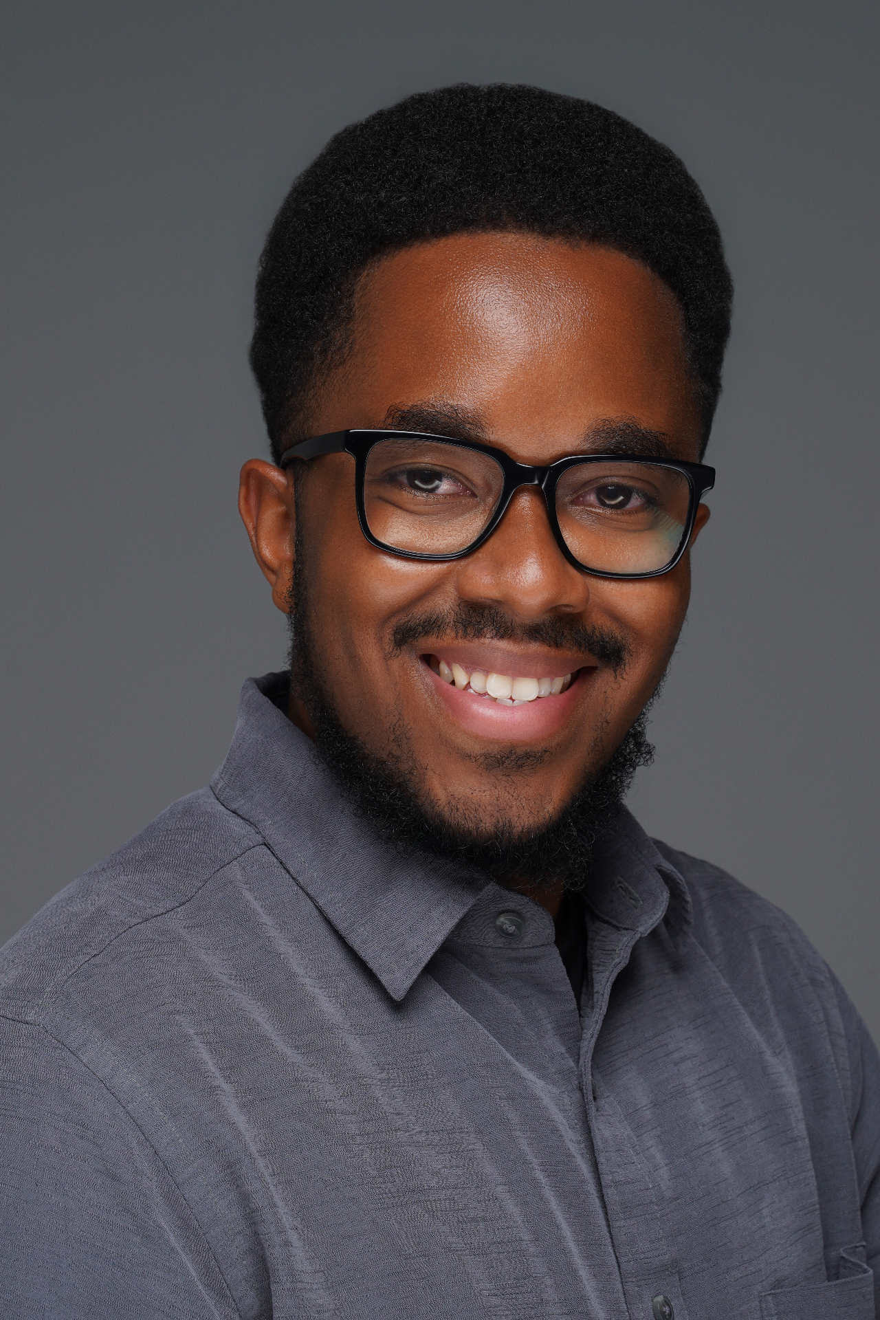 Studio headshot of a smiling man wearing glasses against a gray background